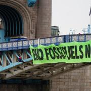 Activists from Extinction Rebellion hang from suspension cords beside a giant banner as they stage a protest on Tower Bridge